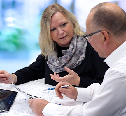 Eine Frau mit schwarzem Pullover und ein Mann im weißen Hemd führen ein Beratungsgespräch