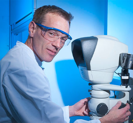 Ein Mann steht in einem Labor und bedient ein Mikroskop. 