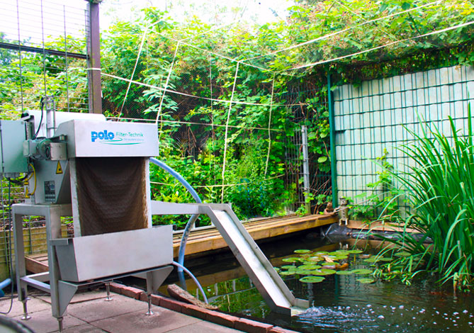 Eine Filteranlage neben einem Teich. Die Filteranlage wird als Teichfilter benutzt.